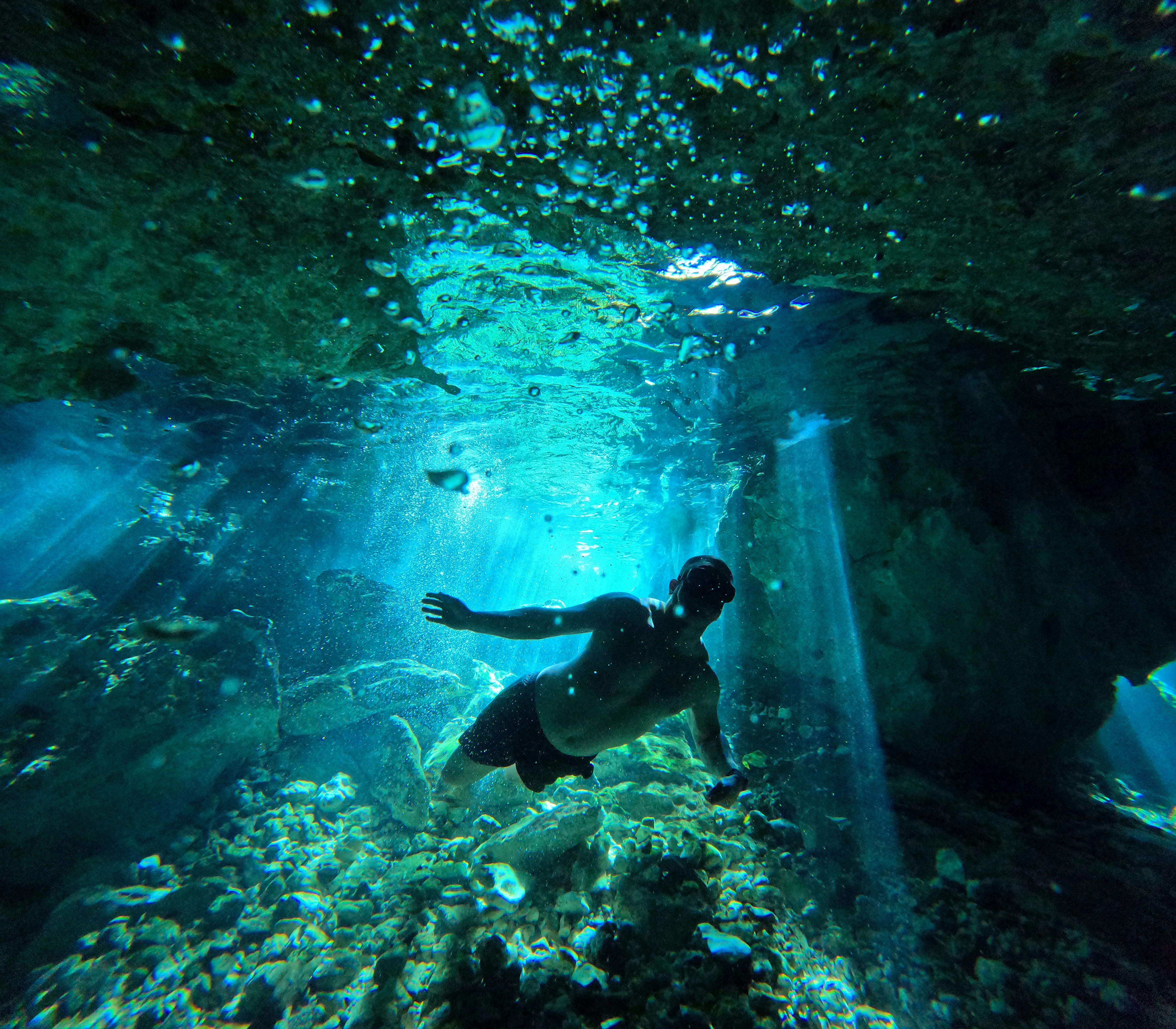A scuba diver silhouetted in a sunlit underwater cave, exploring the depths